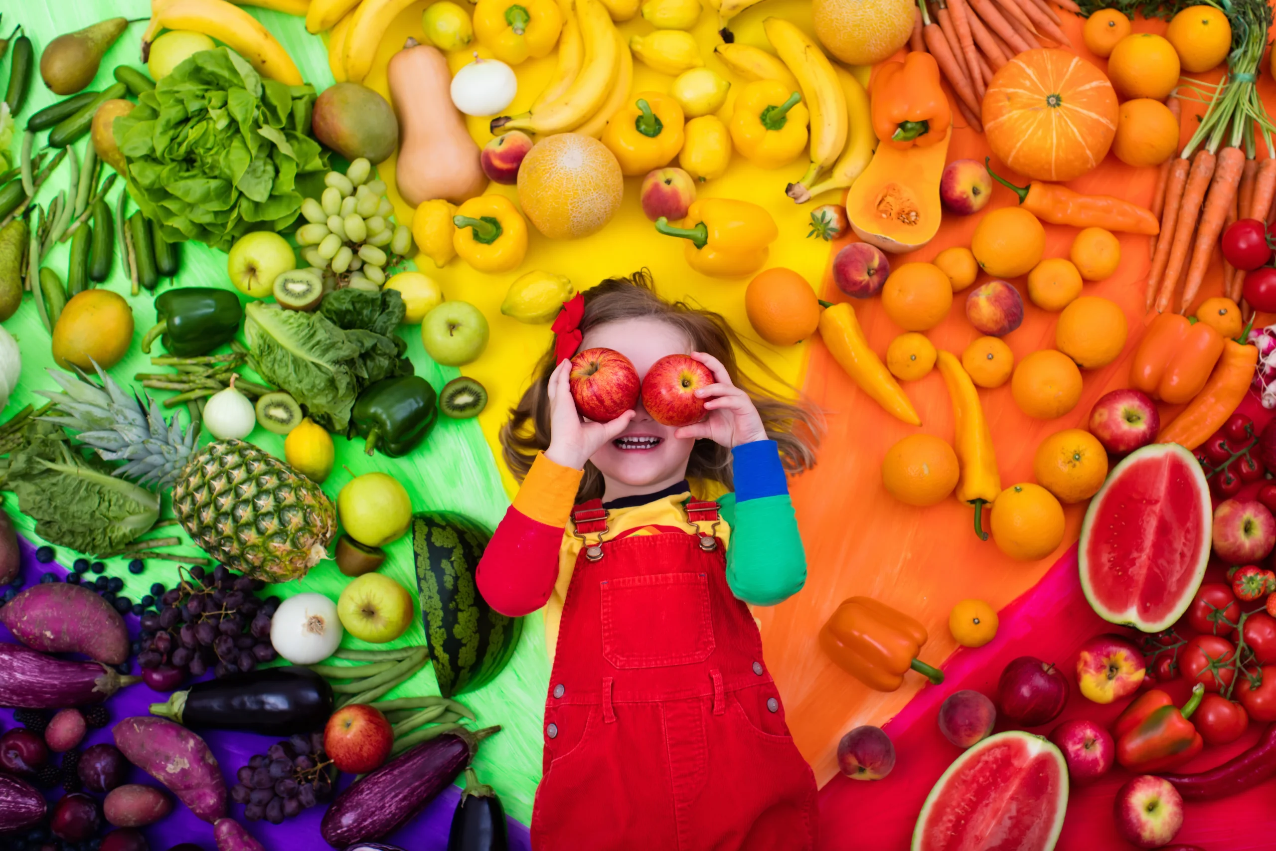 Little girl with variety of fruit and vegetable. Colorful rainbow of raw fresh fruits and vegetables. Child eating healthy snack. Vegetarian nutrition for kids. Vitamins for children. View from above.